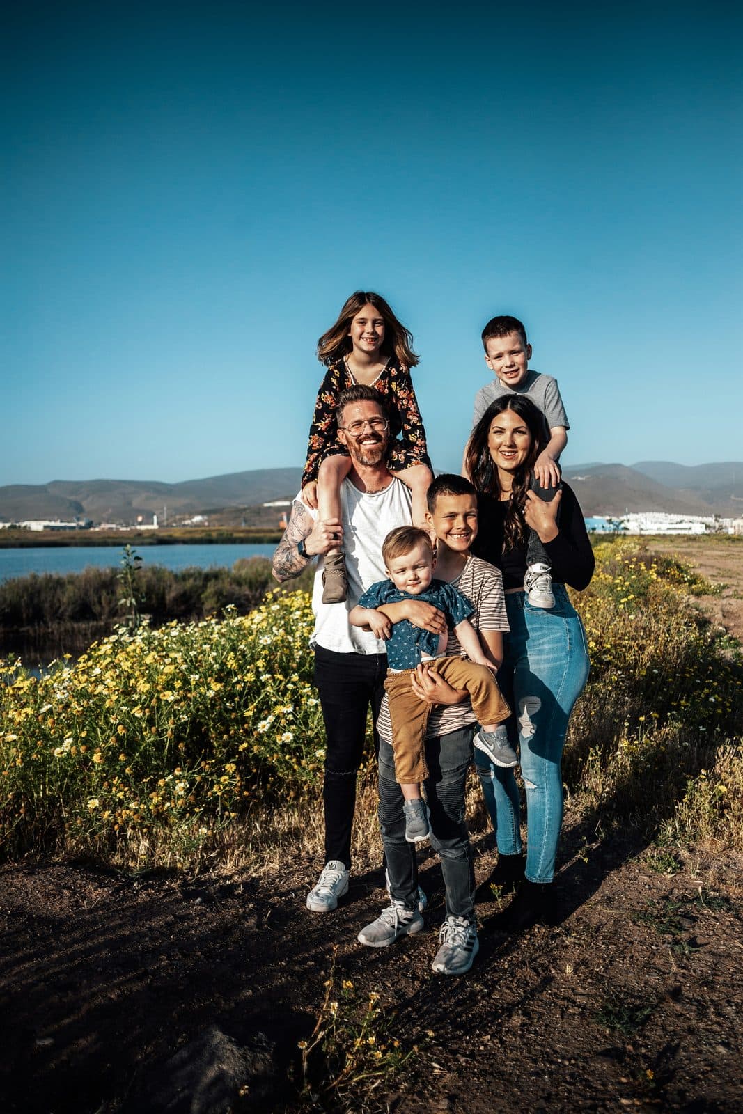A family of six smiling together on a hillside above the coast